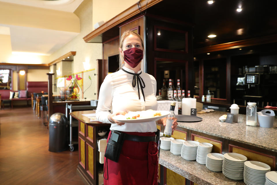 BONN, GERMANY - MAY 12: Waitress Joy at Miebachs restaurant serves a menu to a guest on the day after restaurants and cafes were allowed to reopen for the first time since March in the state of North Rhine-Westphalia on May 12, 2020 in Cologne, Germany. Local governments nationwide are following their own timetables in letting restaurants and cafes reopen this week. The effort is part of a careful easing of restrictions as German authorities seek to raise economic activity while still monitoring the rates of coronavirus infection. (Photo by Andreas Rentz/Getty Images)