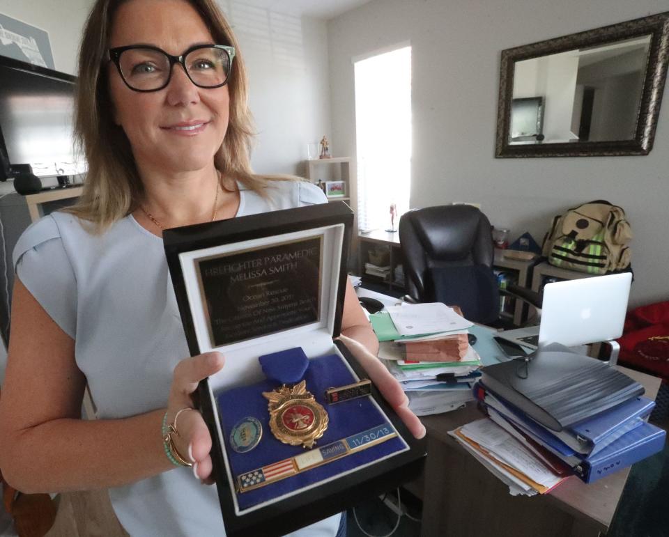 Former New Smyrna Beach Fire Department Lt. Melissa Smith holds her Life Saving Award of Excellence from the department, Wednesday April 17, 2024 next to two large stacks of paperwork from her discrimination lawsuit.