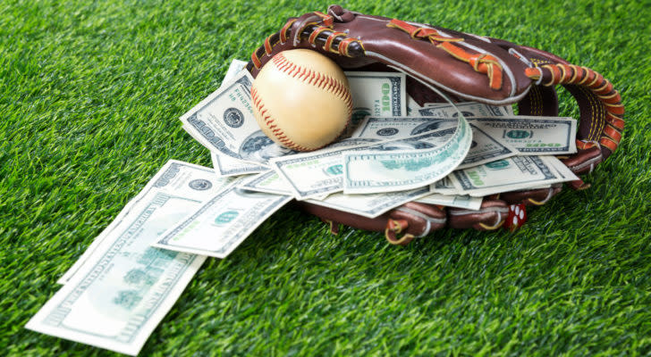 A baseball glove rests on a field with a baseball and several hundred dollar bills inside.