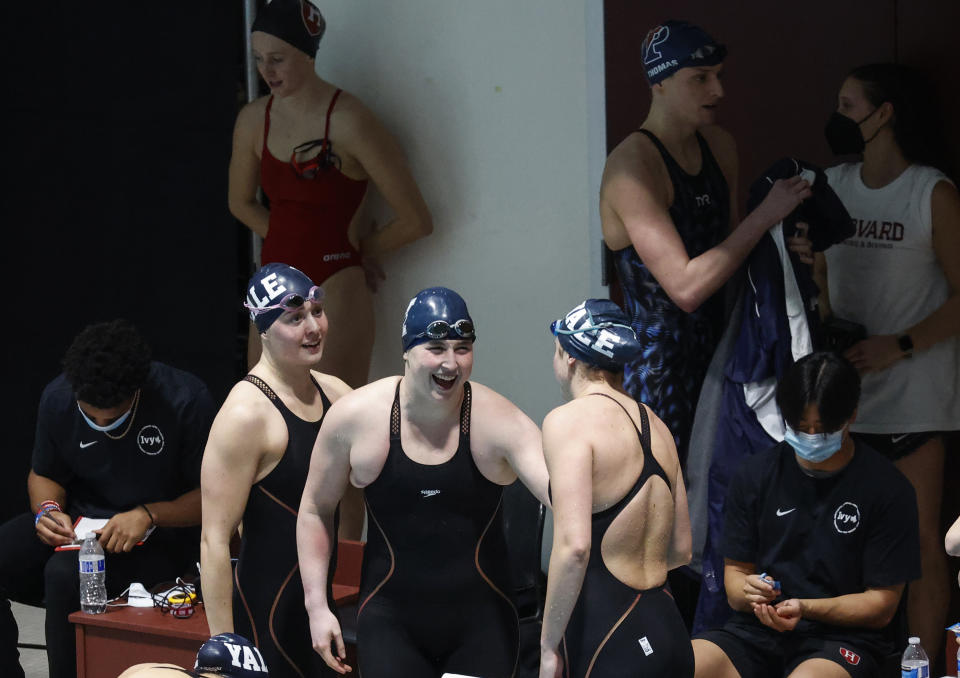 Yale's Iszac Henig, center, celebrates with teammates after the relay team set a meet and pool record in the 200-yard freestyle relay event as Penn's Lia Thomas walks past after the Penn team placed fourth at the Ivy League Women's Swimming and Diving Championships at Harvard University, Thursday, Feb. 17, 2022, in Cambridge, Mass. Henig is transitioning to male but hasn't begun hormone treatments yet and Thomas is transitioning to female. (AP Photo/Mary Schwalm)