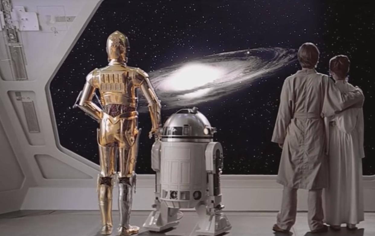 C-3PO stands next to R2D2