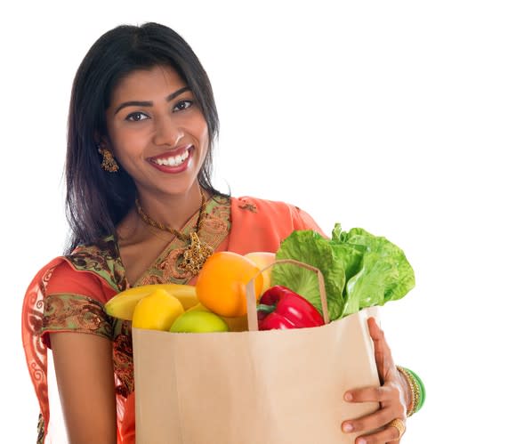 Indian woman smiling carrying bag of groceries.