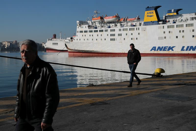 People walk next to a moored passenger ferry during a 24-hour strike at the Port of Piraeus, near Athens