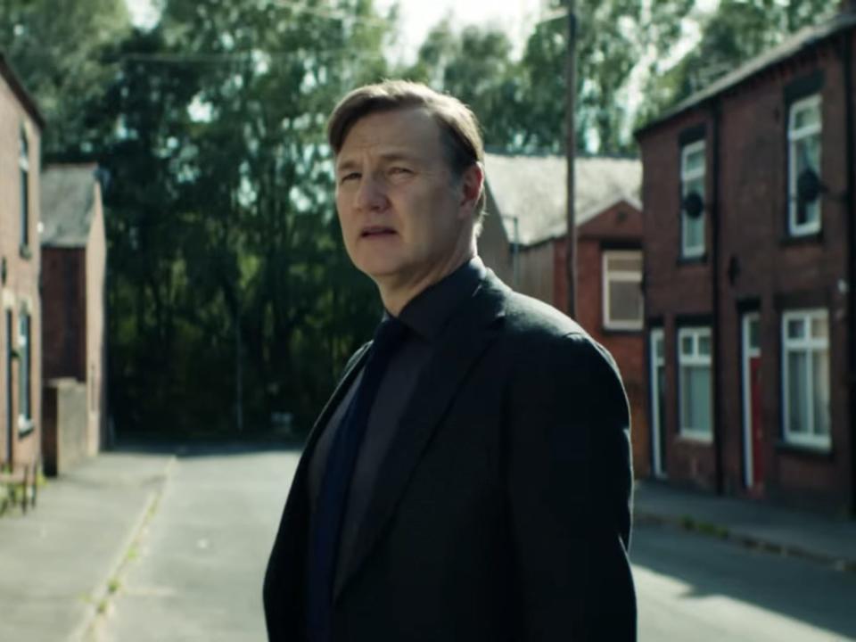 A man in a dark suit stands in a town street.