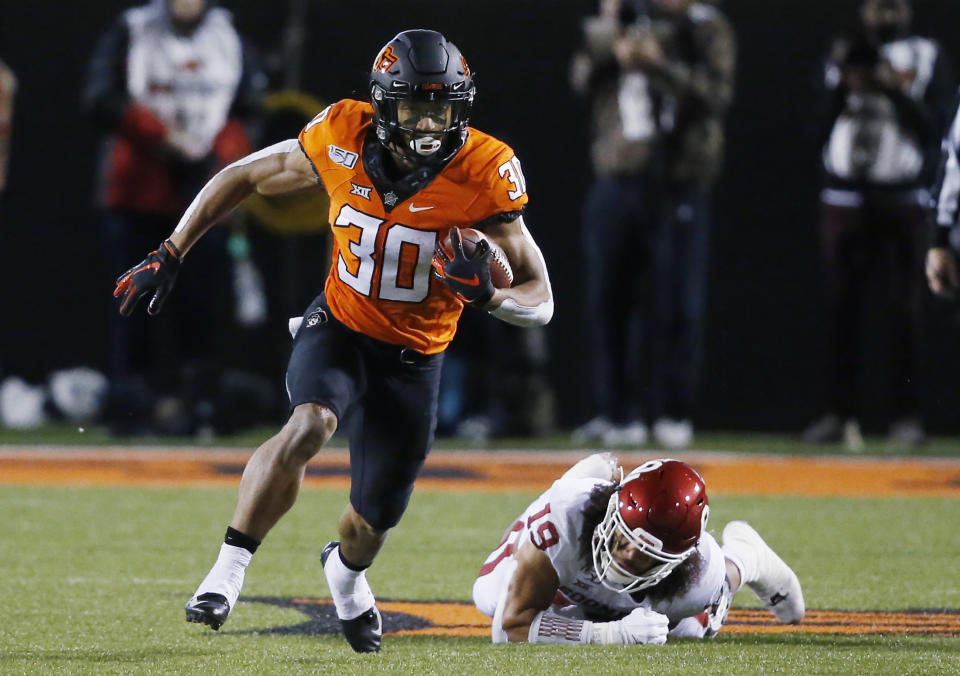 FILE - In this Nov. 30, 2019, file photo, Oklahoma State running back Chuba Hubbard (30) carries past Oklahoma linebacker Caleb Kelly during an NCAA college football game in Stillwater, Okla. Hubbard said on Twitter that he won’t do anything with the program until there is change after coach Mike Gundy was photographed wearing a T-shirt representing far-right online publication One America News Network. Gundy is seen in a photograph on Twitter wearing the T-shirt with the letters OAN. (AP Photo/Sue Ogrocki, File)