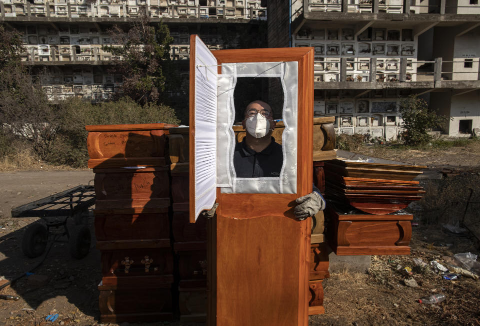 A funeral worker asks for his photo to be taken through one of the used coffins he is moving following cremations at La Recoleta cemetery during the coronavirus pandemic in Santiago, Chile, Monday, April 19, 2021. (AP Photo/Esteban Felix)