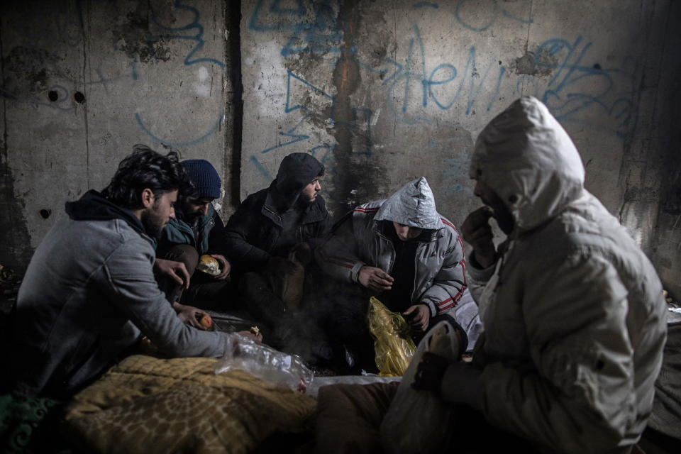 In this picture taken Saturday Dec. 14, 2019, a group of Syrian migrants have breakfast inside an an abandoned building as they take shelter before making another attempt to cross into Croatia in the outskirts of Bihac, northwestern Bosnia.(AP Photo/Manu Brabo)