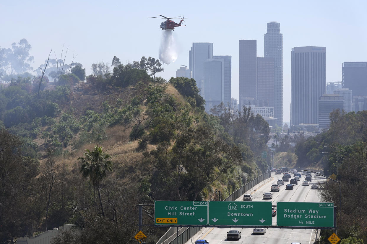 A Los Angeles Fire Department helicopter drops water on a brush fire next to a freeway.