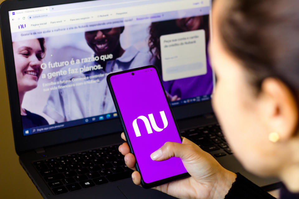 BRAZIL - 2022/04/18: In this photo illustration, a woman holds a smartphone with the Nubank logo displayed on the screen with the Nubank website displayed in the background. (Photo Illustration by Rafael Henrique/SOPA Images/LightRocket via Getty Images)