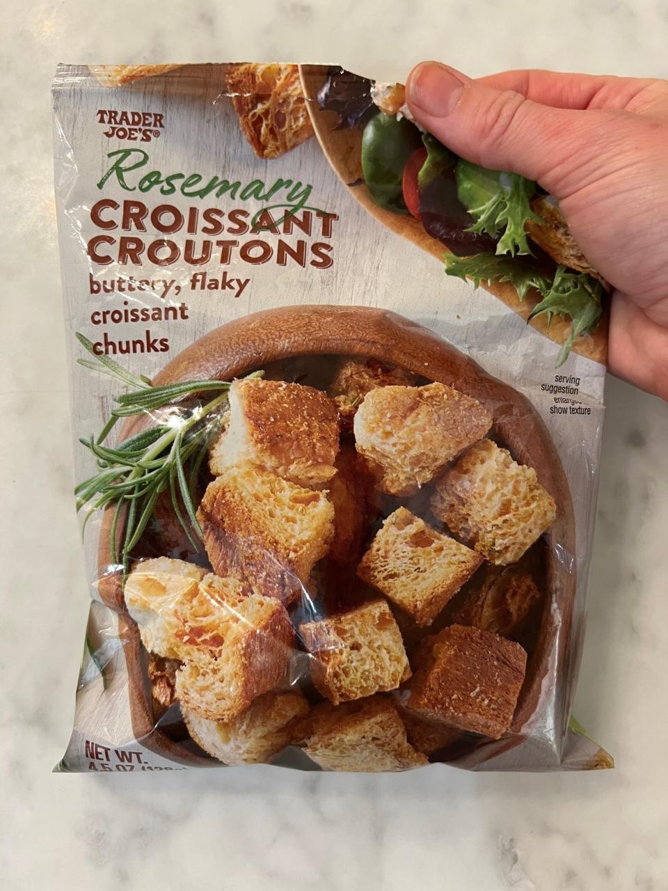 A hand holding a bag of Rosemary Croissant Croutons.