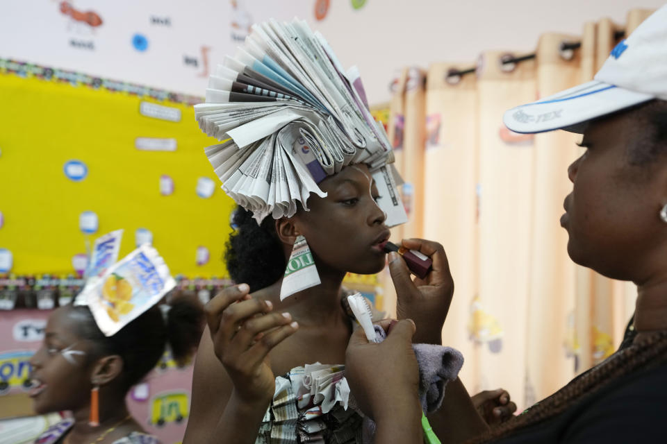 Maureen Okoduwa left, wearing an outfit made from recycled newspapers, receives makeup back stage before a 'trashion show' in Sangotedo Lagos, Nigeria, Saturday, Nov. 19, 2022. (AP Photo/Sunday Alamba)