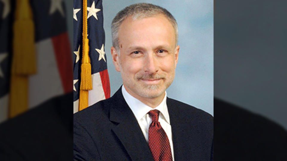 Headshot of James Baker with American flag in background.