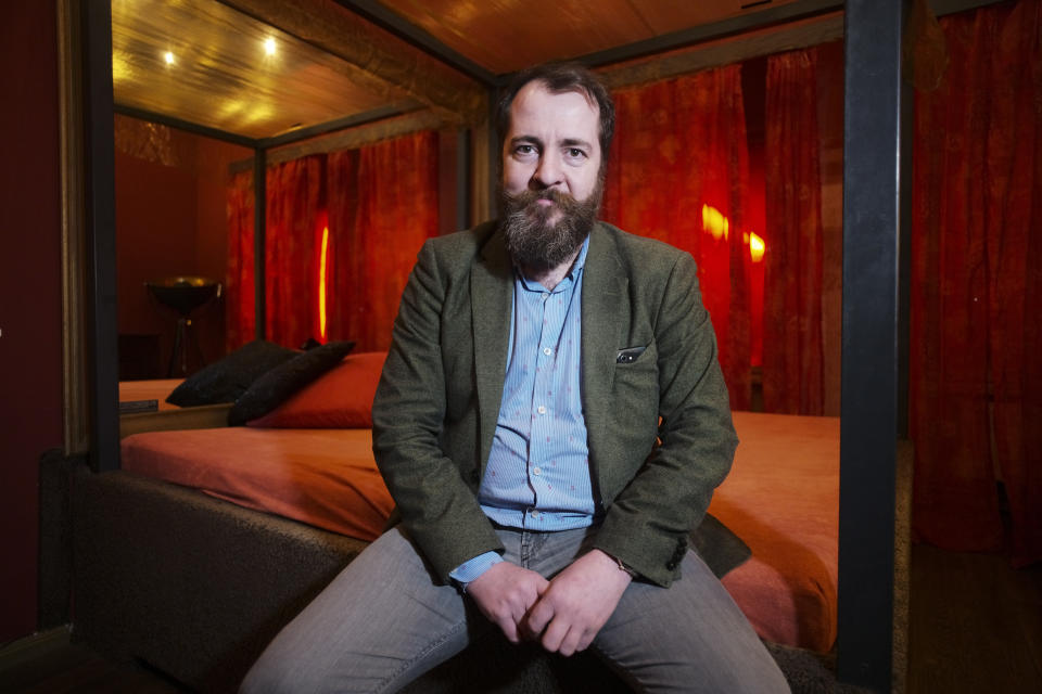 Aurel Johannes Marx sits on a bed in his three room brothel 'Lankwitzer 7' as he poses for photo after and interview with the Associated Press in Berlin, Germany, Friday, March 13, 2020. Sex for sale has long been a staple part of the German capital's hedonistic nightlife, but amid concerns over the new coronavirus even the world's supposedly oldest profession is being hit by a sudden slump. For some, especially older adults and people with existing health problems, it can cause more severe illness, including pneumonia. (AP Photo/Markus Schreiber)