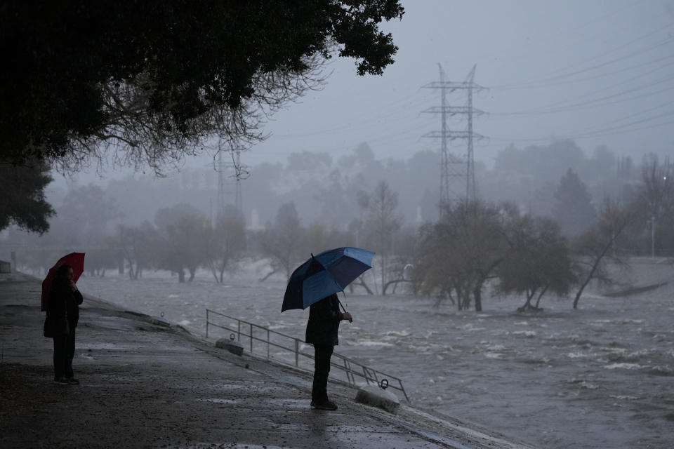 A couple walks on the edge of the Los Angeles River, carrying stormwater downstream Sunday, Feb. 4, 2024, in Los Angeles. The second of back-to-back atmospheric rivers battered California, flooding roadways and knocking out power to hundreds of thousands and prompting a rare warning for hurricane-force winds as the state braced for what could be days of heavy rains. (AP Photo/Damian Dovarganes)