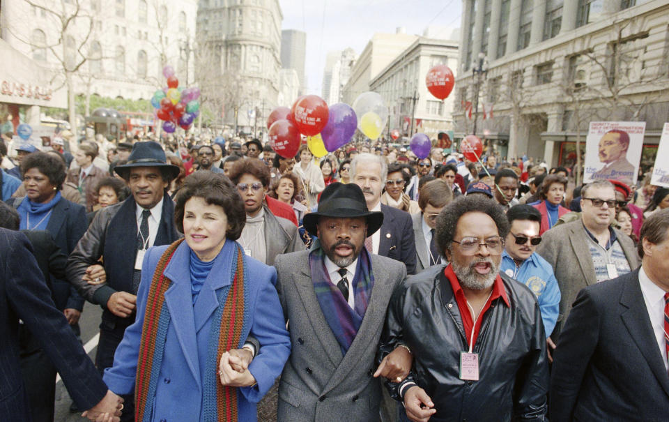 FILE - Dianne Feinstein, front left, California Assembly Speaker Willie Brown, center, and The Rev. Cecil Williams of the Glide Memorial Church of San Francisco, hold hands during the Dr. Martin Luther King Jr. march in downtown San Francisco, Jan. 20, 1986. About 60,000 people attended the rally, which ended at the San Francisco Civic Center. (AP Photo/Paul Sakuma, File)