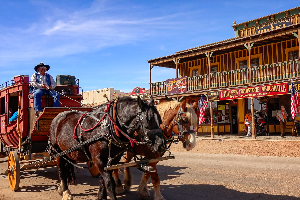 Stagecoach pulled by two horses down a street in Tombstone, Arizona, old western style buildings line in the background, a blue sky in the background