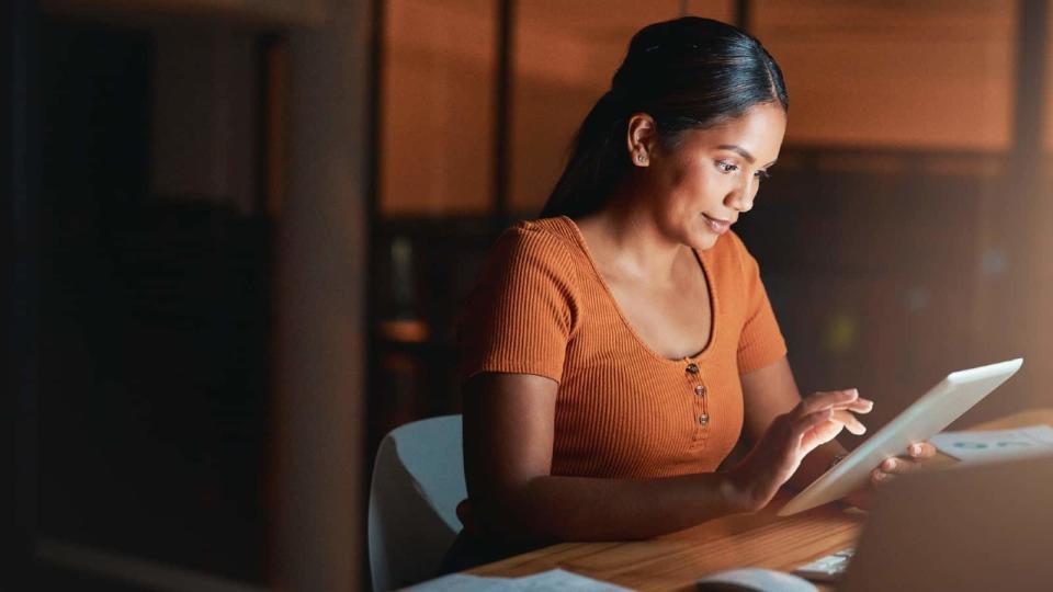 Shot of an young Indian businesswoman sitting alone in the office at night and using a digital tablet