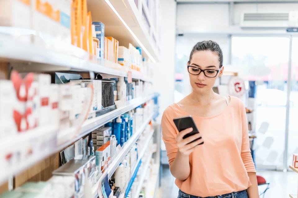 A woman in a pharmacy looks at her phone