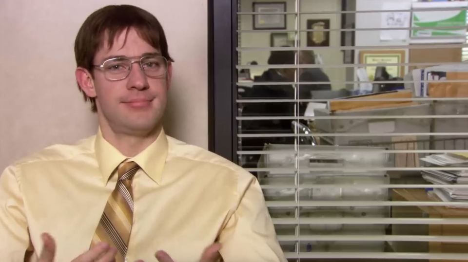 Man in office setting wearing a yellow shirt and tie, looking at the camera with a slight smile