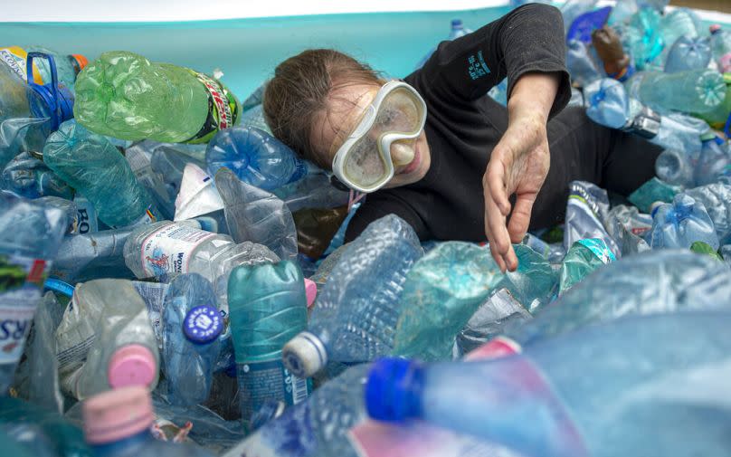 An activist simulates swimming in an inflatable pool filled with plastic PET bottles during a protest outside the Ministry of Environment in Bucharest, June 2021