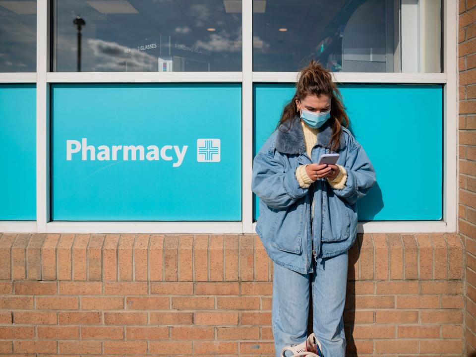 Person standing outside pharmacy looking at cell phone