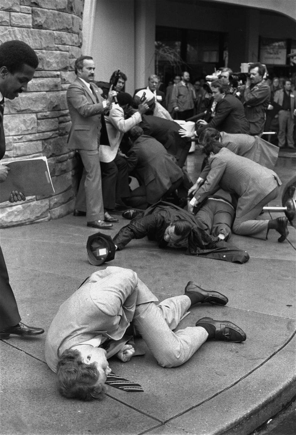 FILE - In this March 30, 1981, file photo, Secret Service agent Timothy J. McCarthy, foreground, Washington policeman Thomas K. Delehanty, center, and presidential press secretary James Brady, background, lie wounded on a street outside a Washington hotel after shots were fired at U.S. President Ronald Reagan. Lawyers for John Hinckley Jr., the man who tried to assassinate Reagan, are scheduled to argue in court Monday, Sept. 27, 2021, that the 66-year-old should be freed from restrictions placed on him after he moved out of a Washington hospital in 2016. (AP Photo/Ron Edmonds, File)