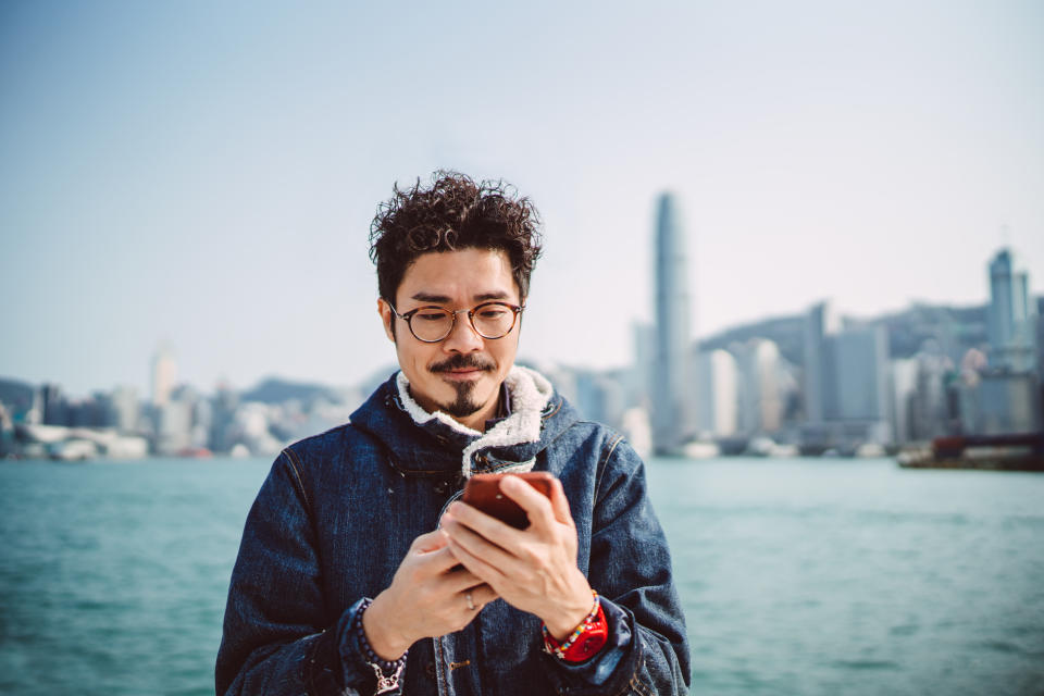 Young asian handsome man using smartphone joyfully in promenade