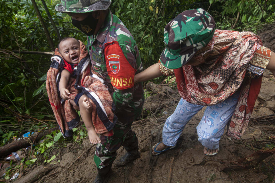 An Indonesian soldier assists a woman to carry her baby as they make their way through an area affected by earthquake-triggered landslide near Mamuju, West Sulawesi, Indonesia, Saturday, Jan. 16, 2021. Damaged roads and bridges, power blackouts and lack of heavy equipment on Saturday hampered Indonesia's rescuers after a strong and shallow earthquake left a number of people dead and injured on Sulawesi island. (AP Photo/Yusuf Wahil)