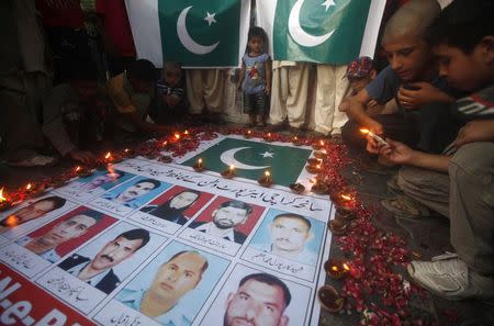 Children light candles in front of a poster with pictures of the members of Airport Security Force (ASF) who were killed on Sunday's Taliban attack on Jinnah International Airport, to commemorate them, in Karachi June 11, 2014. REUTERS/Athar Hussain