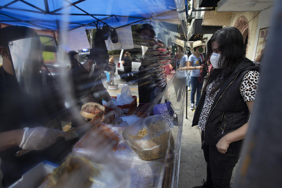 A vendor, wearing a face shield and protective face mask amid the new coronavirus pandemic, prepares a "torta de chilaquiles" for a customer, in Mexico City, Saturday, Aug. 1, 2020. More than half of Mexicans work in the informal economy, which is believed to have shed many more jobs as the economic shutdown caused by the COVID-19 pandemic has driven the country deeper into a recession. (AP Photo/Marco Ugarte)