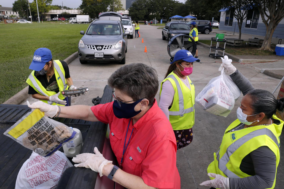 Volunteers load bags of food into the bed of a client's pick up truck in the drive thru line at the West Houston Assistance Ministries Wednesday, Oct. 14, 2020, in Houston. Demand for food in the Houston area, long subjected to the volatility of the oil industry, will probably continue without more government relief for jobless workers, said Mark Brown, CEO of WHAM which gives food to nearly 2,000 people each week. (AP Photo/Michael Wyke)