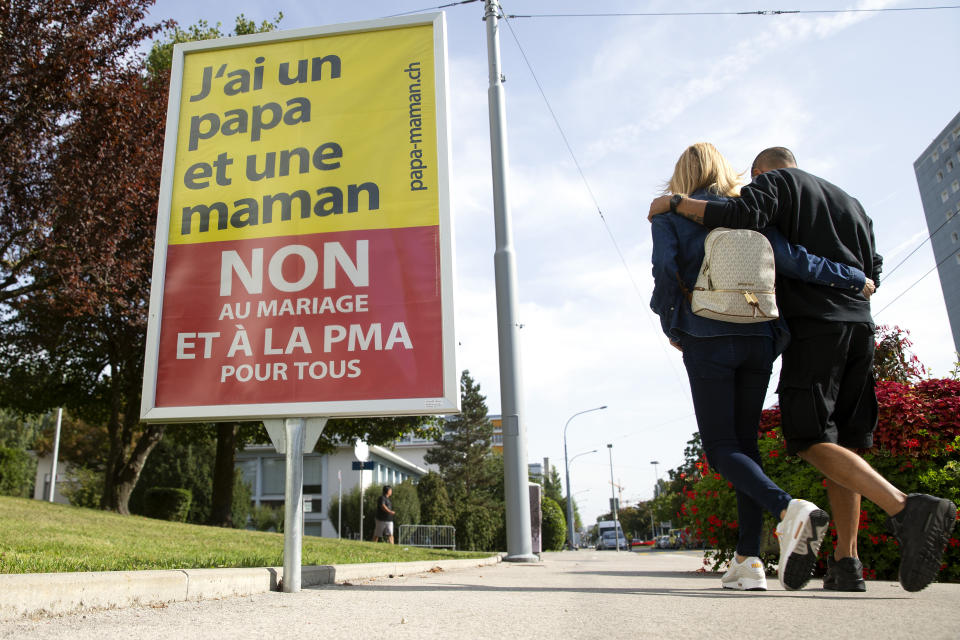 A couple walk past a poster showing a slogan in Perly near Geneva, Saturday Sept. 25, 2021. Voters in Switzerland will decide Sunday whether to allow same-sex marriages in the rich Alpine country, one of the few in Western Europe where gay and lesbian couples do not already have the right to wed. Opponents have argued that replacing civil partnerships with full marriage rights somehow would undermine families based on a union between one man and one woman. (Salvatore Di Nolfi/Keystone via AP)