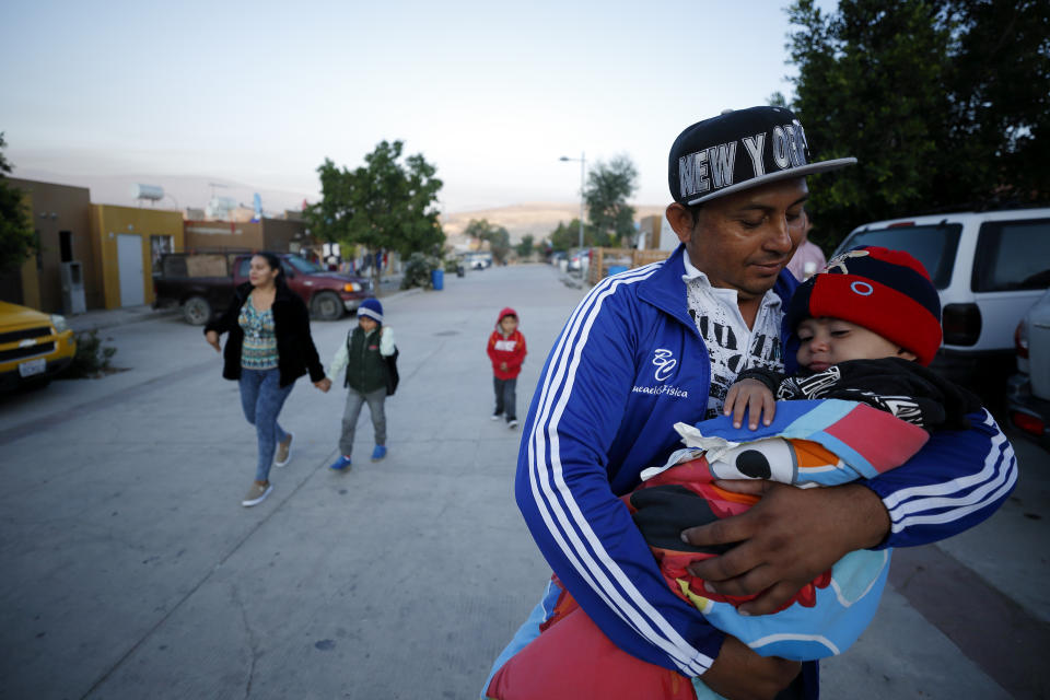 In this July 10, 2019, photo, Juan Carlos Perla carries his youngest son, Joshua Mateo Perla, as the family leaves their home in Tijuana, Mexico, for an asylum hearing in San Diego. They were among the first sent back to Mexico under a Trump administration policy that dramatically reshaped the scene at the U.S.-Mexico border by returning migrants to Mexico to wait out their U.S. asylum process. (AP Photo/Gregory Bull)