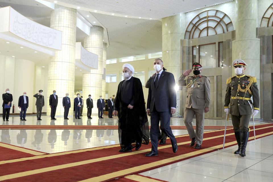 In this photo released by the official website of the office of the Iranian Presidency, Iraqi Prime Minister Mustafa al-Kadhimi, center, is welcomed by President Hassan Rouhani, center left, as they wear protective face masks to help prevent spread of the coronavirus, during an official arrival ceremony, in Tehran, Iran, Tuesday, July 21, 2020. (Iranian Presidency Office via AP)