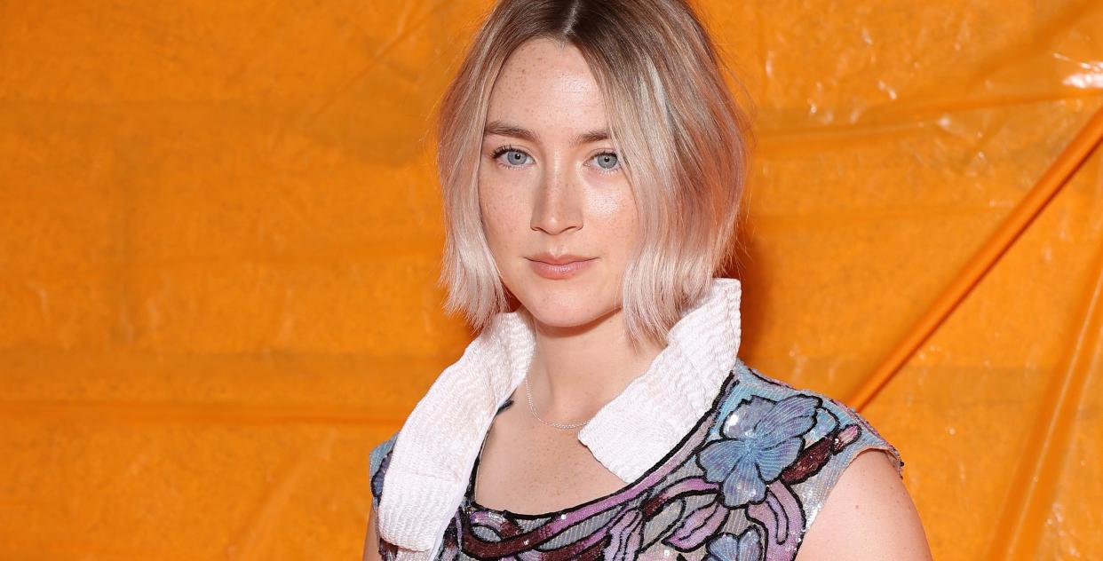 saoirse ronan, a woman with blond hair in a bob stands looking at the camera wearing a floral sequin dress