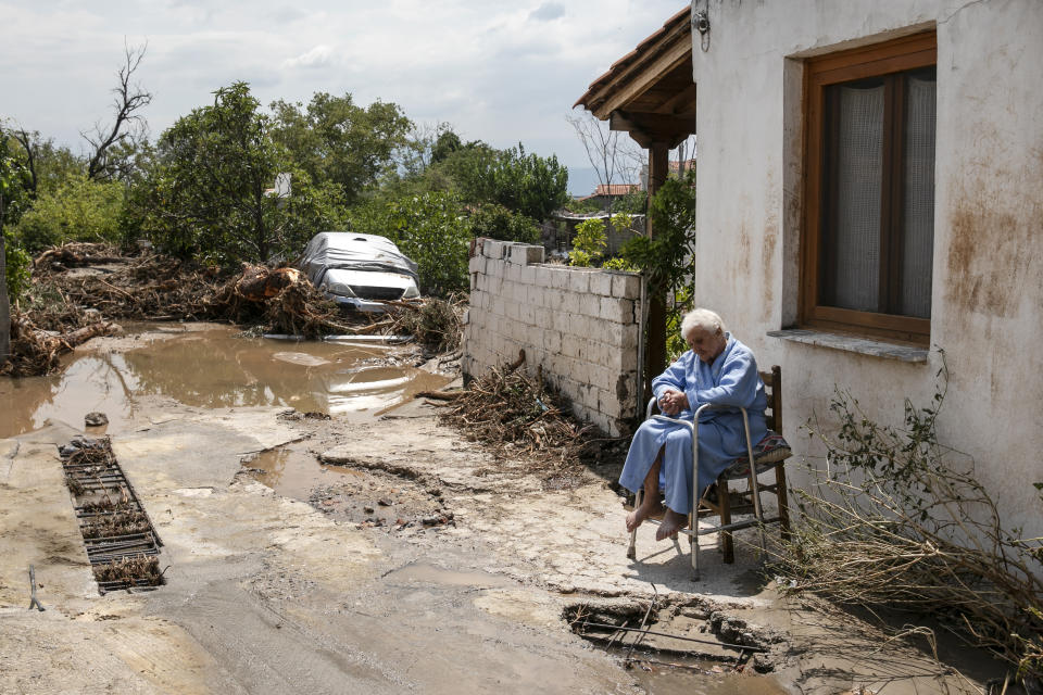 A woman sits outside her home following a storm at the village of Politika, on Evia island, northeast of Athens, on Sunday, Aug. 9, 2020. Five people have been found dead and dozens have been trapped in their homes and cars from a storm that has hit the island of Evia, in central Greece, police say. (AP Photo/Yorgos Karahalis)