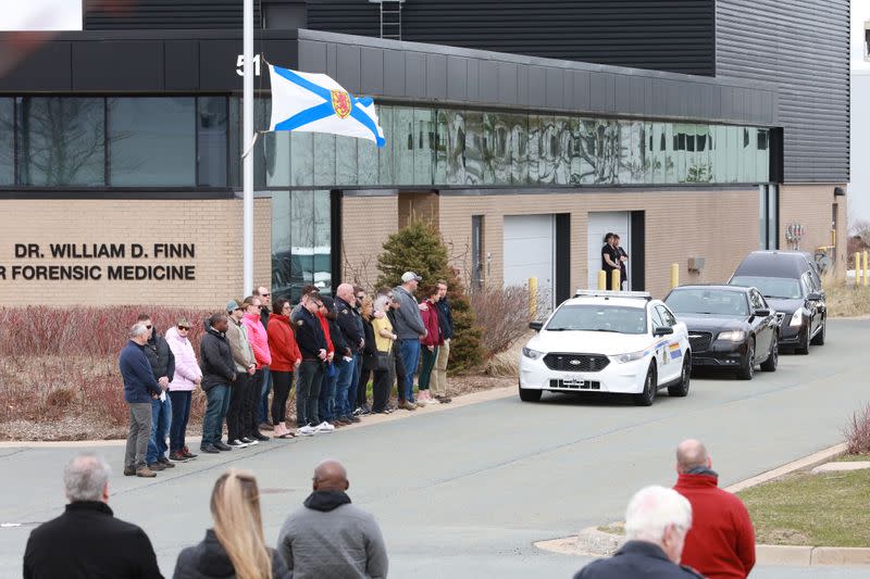 People stand under a provincial flag at half mast prior to a procession for RCMP Constable Heidi Stevenson