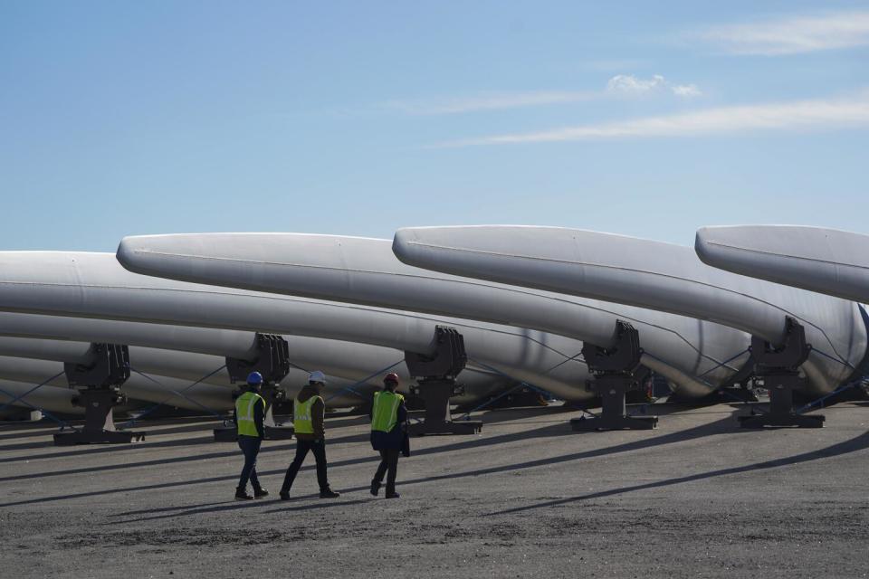 Workers walk beneath a row of giant wind turbine blades.