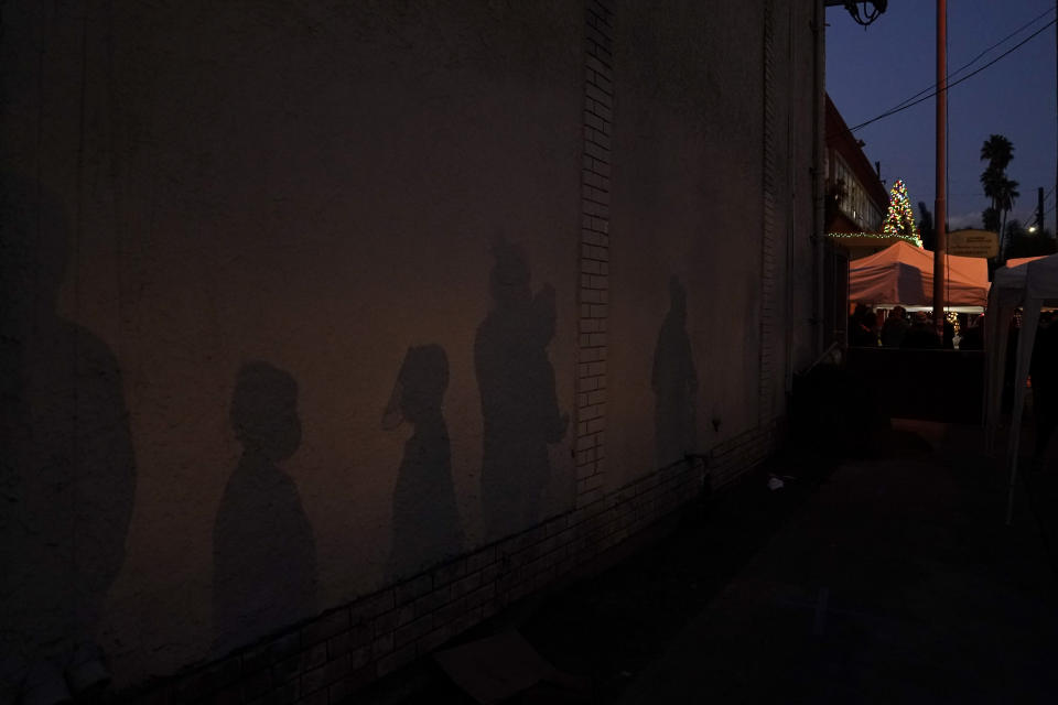 FILE - In this Dec. 17, 2020, file photo shadows of people are cast on a building while they wait to get food and toys at Los Angeles Boys & Girls Club in the Lincoln Heights neighborhood of Los Angeles. According to a survey from The Associated Press-NORC Center for Public Affairs Research that also finds some Americans are feeling a bit sadder, lonelier and less grateful than last year.(AP Photo/Jae C. Hong, File)