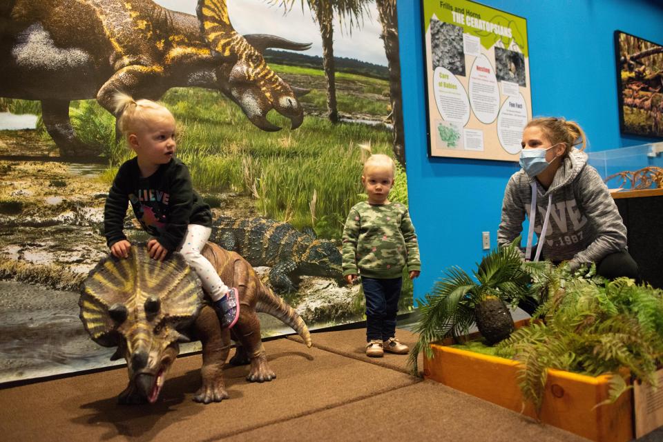 Twins Quinlyn, left, and Bexley, 1, are helped onto a triceratops baby model by their mom, Kayla Christian, at an exhibit at the Kansas Children&#39;s Discovery Center, which participates in Sunflower Summer.