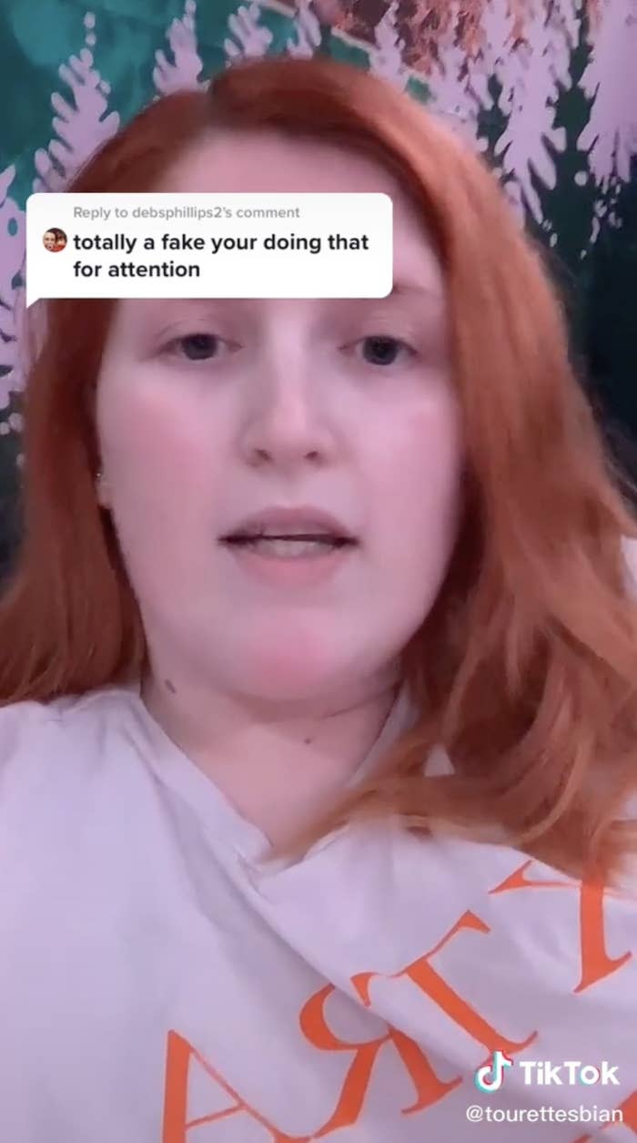 Screenshot of a TikTok from @tourettesbian featuring a young person with red hair and a reply saying "totally a fake your [sic] doing that for attention"