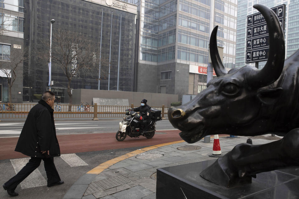 In this photo taken Thursday, Feb. 13, 2020, a man walks past a bull sculpture on a quiet street Beijing, China. Millions of Chinese workers and entrepreneurs are bearing the rising costs of an anti-virus campaign that has shut down large sections of the economy. The government has imposed restrictions nationwide that have stalled travel and sales of real estate and autos. (AP Photo/Ng Han Guan)