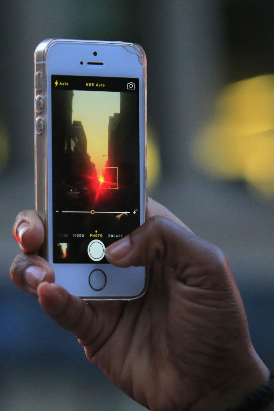 A man takes a picture of a sunset, during the bi-annual occurrence "Manhattanhenge" in New York