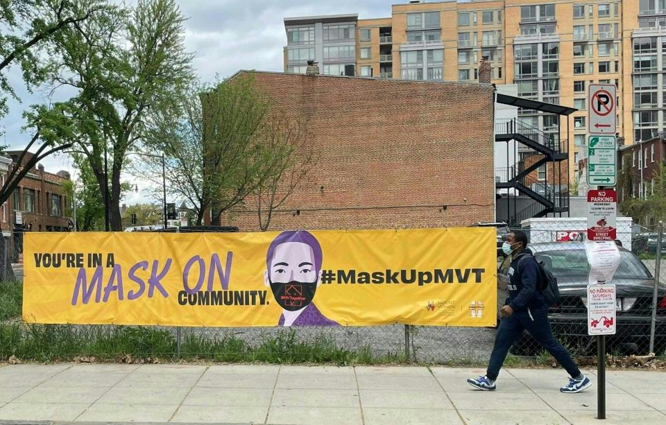 A person wearing a mask walks by a banner encouraging the use of face coverings in Washington, DC on April 16, 2021.