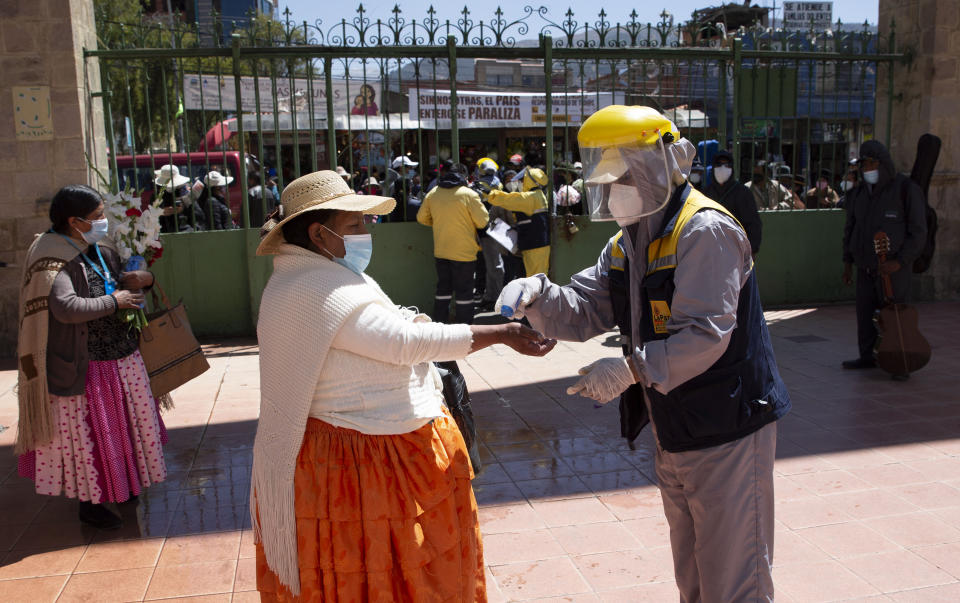 Un trabajador toma la temperatura de una mujer para evitar la propagación del nuevo coronavirus en la entrada del Cementerio General de La Paz, Bolivia, el miércoles 23 de septiembre de 2020. (AP Foto/Juan Karita)