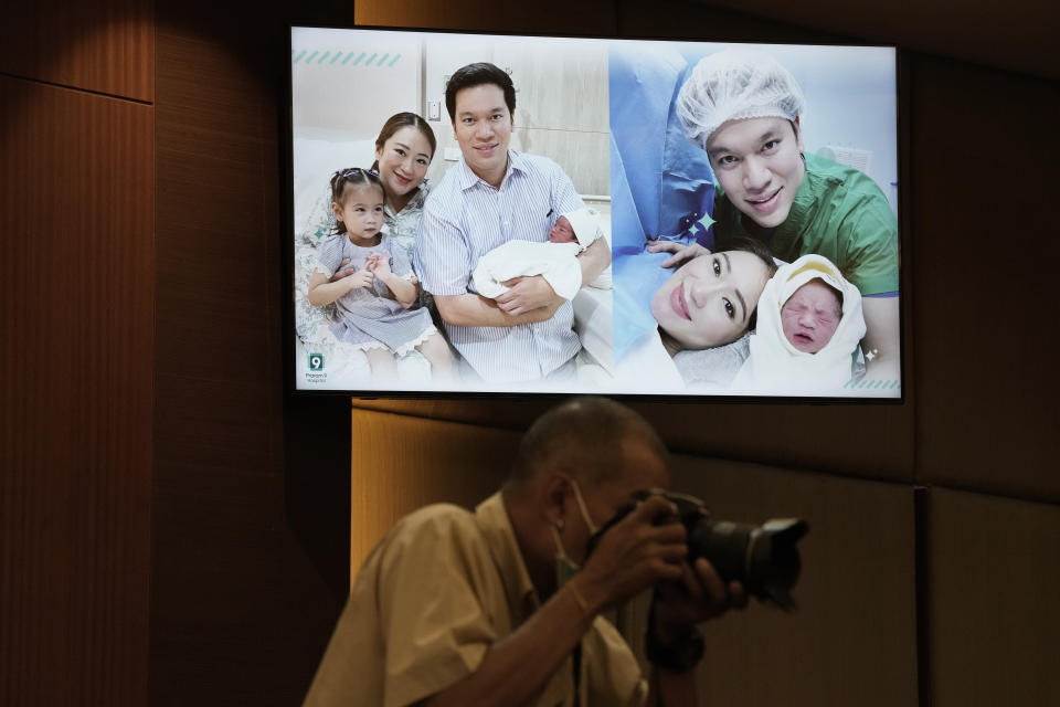 A Thai photographer takes picture under television showing Paetongtarn Shinawatra, Pheu Thai party's top politician and youngest daughter of exiled former deposed Thai leader Thaksin Shinawatra and her husband Pidok Sooksawas with her new born son at press conference in Bangkok, Thailand, Wednesday, May 3, 2023. The frontrunning candidate for prime minister of Thailand said Wednesday she’s eager to get back on the campaign trail, just two days after giving birth. (AP Photo/Sakchai Lalit) (AP Photo/Sakchai Lalit)
