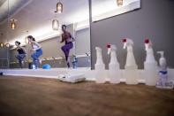 Cleaning products line the wall as Mariam Sufi, left, Lara Atella, second from left, and Lashone Wilson, right, hold an online yoga class via webcam at Hot Yoga Capitol Hill on H Street in Northeast Washington, March 18, 2020. (AP Photo/Andrew Harnik)