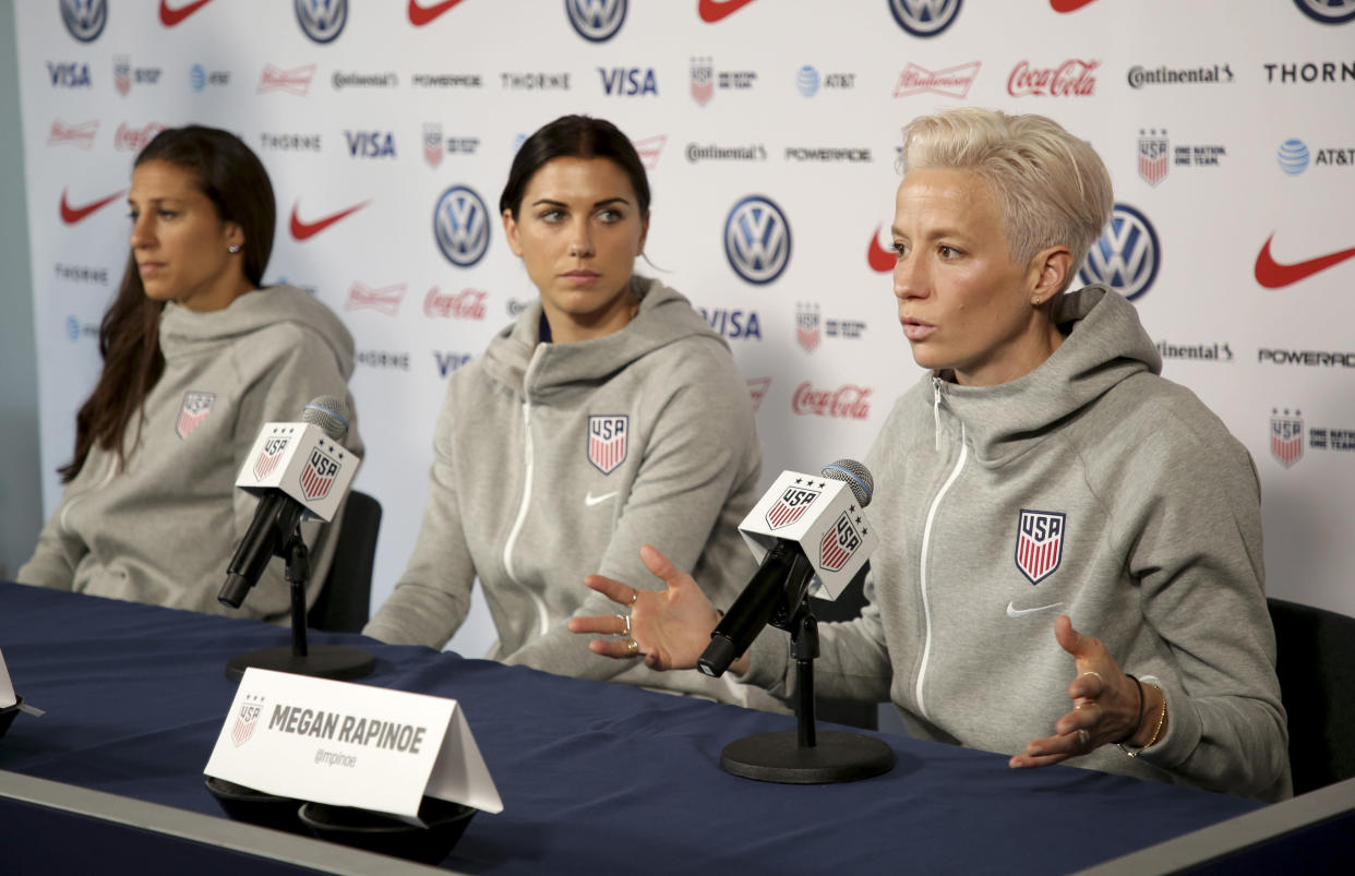 United States women's national soccer team members, from left, Carli Lloyd and Alex Morgan listen as teammate Megan Rapinoe speak to reporters during a news conference in New York, Friday, May 24, 2019. (AP Photo/Seth Wenig)