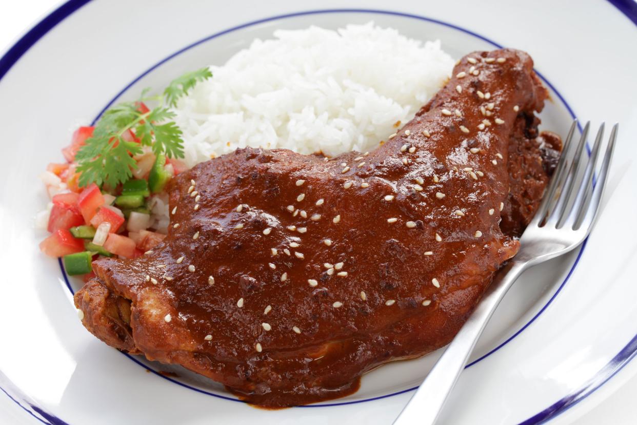 Closeup of turkey mole with white rice and salsa on a blue-lined white plate with a fork