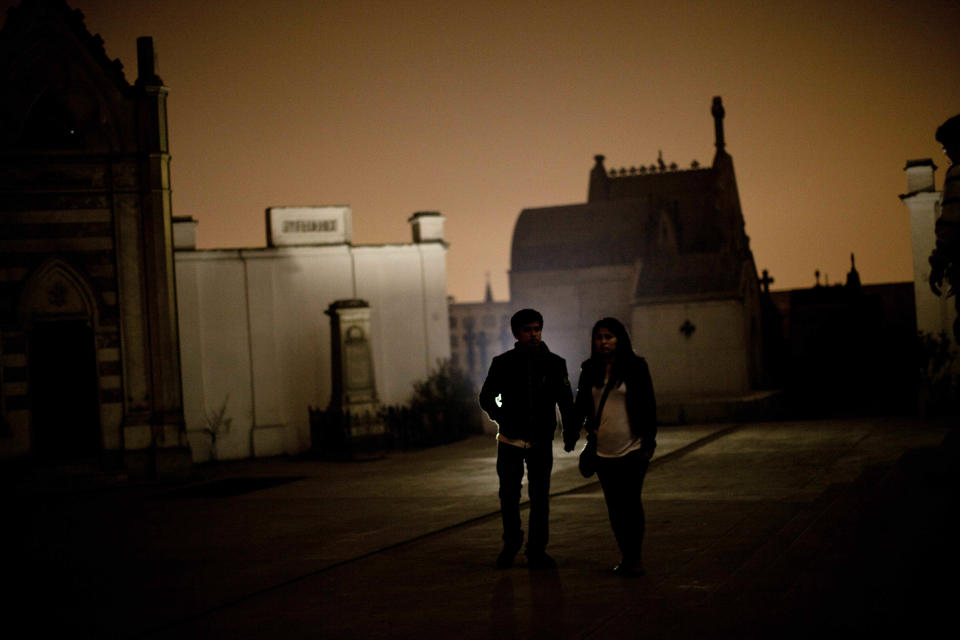 In this Nov. 10, 2012 photo, a couple holds hands as they take a nighttime guided tour through the Presbitero Matias Maestro cemetery in Lima, Peru. Visitors to the 54-acre cemetery just 20 blocks from Lima's presidential palace, one of Latin America's oldest, are treated to tales about the people buried here in a three-hour, nighttime guided tour run by its owner, Beneficiencia de Lima (AP Photo/Rodrigo Abd)